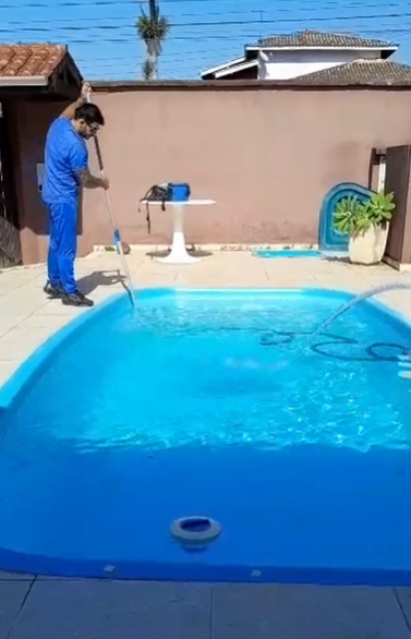 Piscineiro Rai aspirando piscina residencial em Caraguatatuba após limpeza completa no Indaiá.